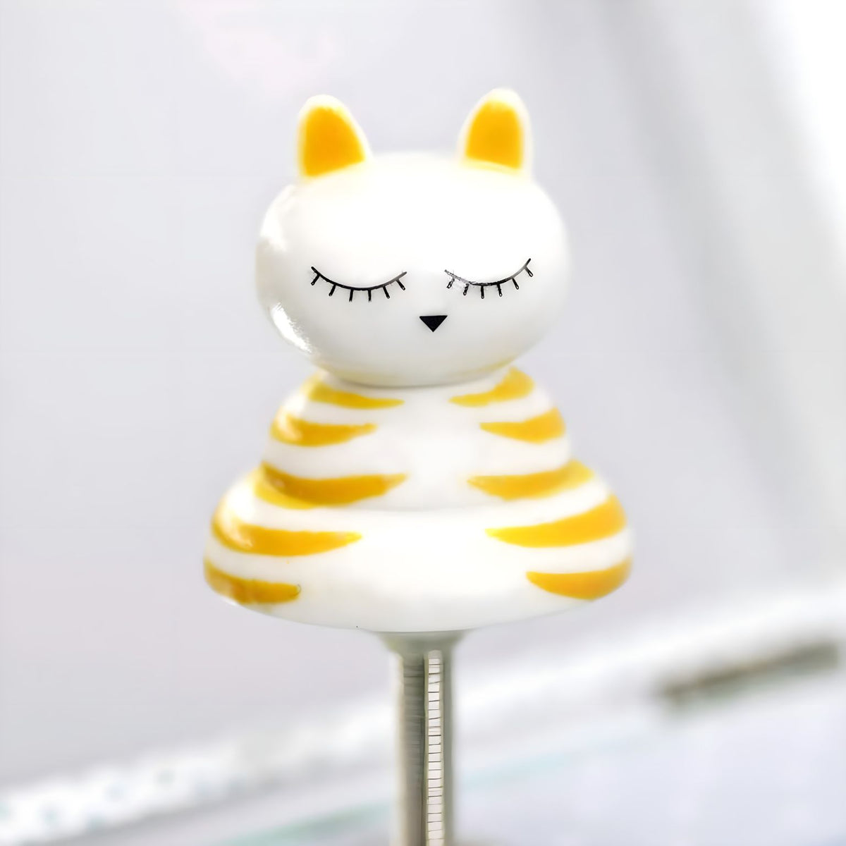 Detalle de la figura del Gato Bailarín, blanca con rayas amarillas y ojos cerrados