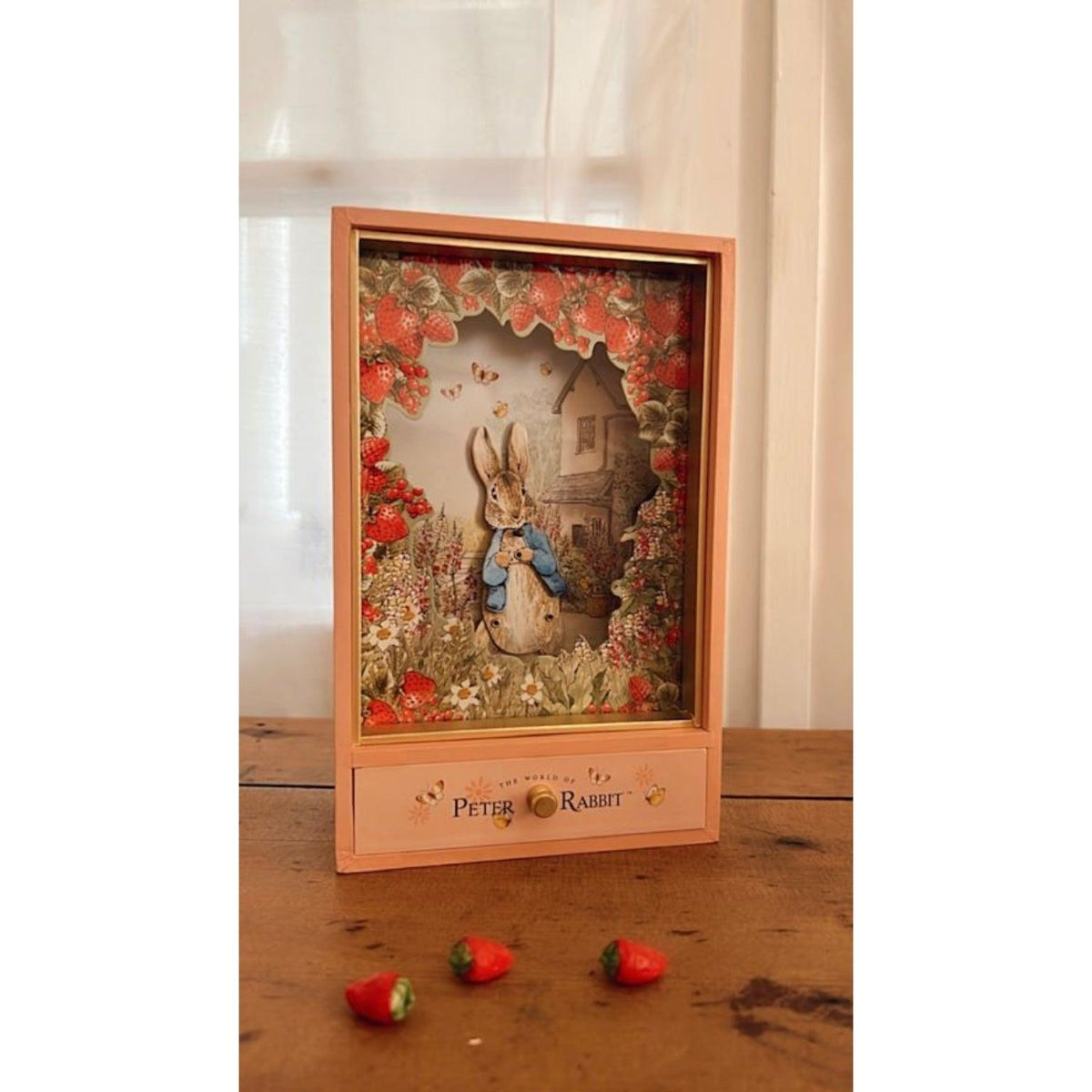 Caixa musical Peter Rabbit Morangos sobre uma mesa, com a figura do coelho e a gaveta fechada