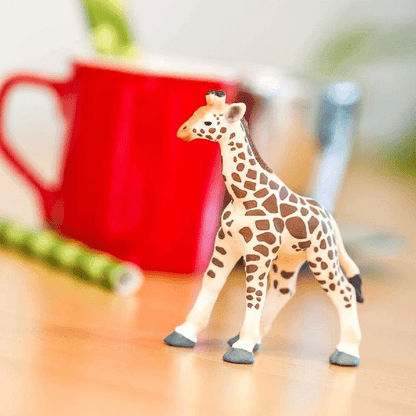 Figura de borracha Girafa bebé sobre mesa de madeira com caneca vermelha